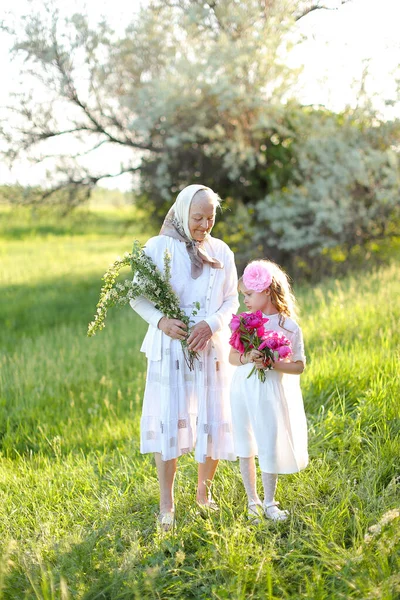 Old happy granny standing with little granddaughter and keeping flowers. — Stock Photo, Image