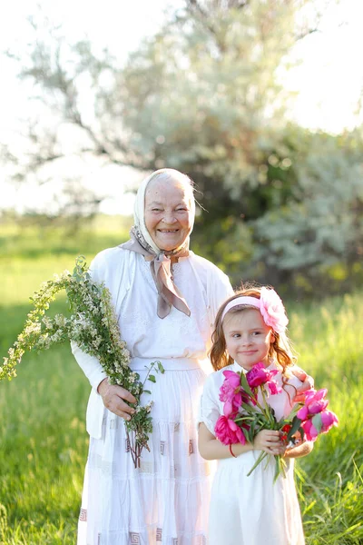 Velha avó americana de pé com a pequena neta e mantendo flores. — Fotografia de Stock