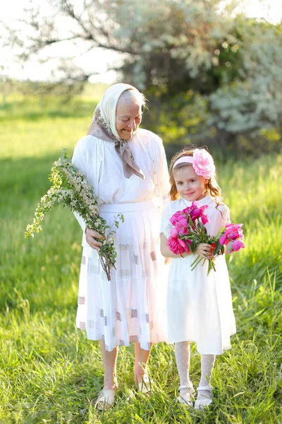 Velha avó de pé com a pequena neta e mantendo flores. — Fotografia de Stock