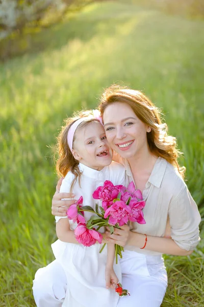 Portrait of happy young mother sitting with little daughter on grass. — Stock Photo, Image