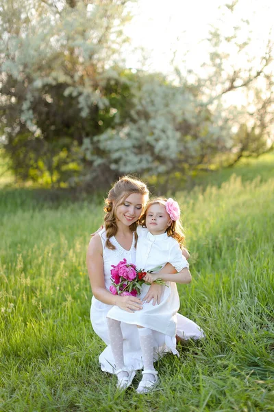 Poirtrait of pretty caucasian mother sitting with little daughter on grass. — Stock Photo, Image