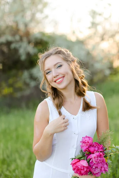 Νεαρό ωραίο κορίτσι με λουλούδια μπουκέτο φορώντας λευκό φόρεμα έξω. — Φωτογραφία Αρχείου