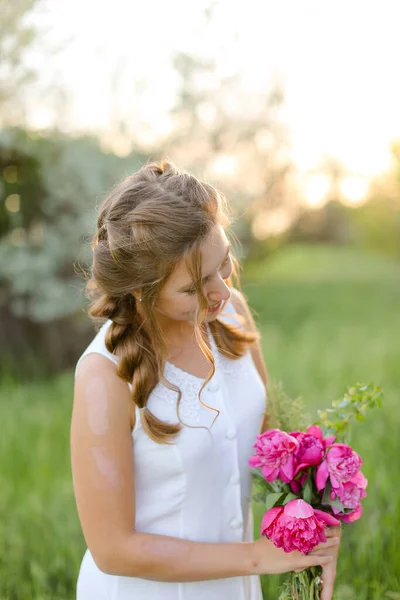Young girl looking at bouquet flowers and wearing white dress outside. — Stock Photo, Image