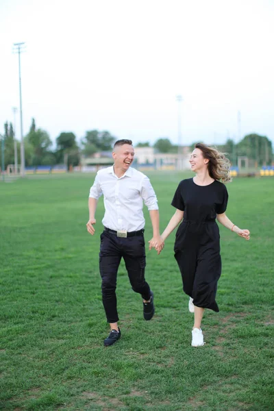 Χαμογελώντας άνδρας και γυναίκα τρέχει στο γήπεδο ποδοσφαίρου και κρατώντας τα χέρια. — Φωτογραφία Αρχείου