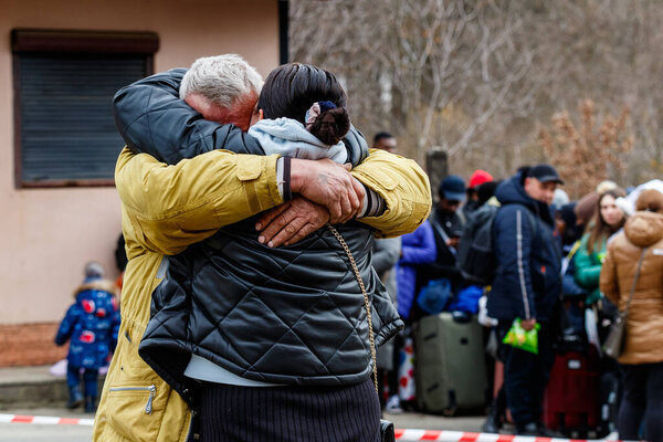Uzhhorod, Ukraine - February 26, 2022: A man on the background of Ukrainian refugees says goodbye to his wife who is fleeing Russian aggression. Refugees on the Ukrainian-Slovak border.