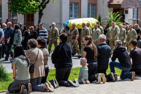 Velykyi Bereznyi, Ukraine - May 11, 2022: Little girl among the locals kneels before the funeral ceremony of a Ukrainian soldier who died in battle with the russian aggressor.