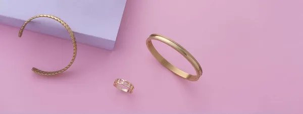 Foto panorámica de pulseras doradas modernas y anillo sobre fondo rosa con espacio para copiar —  Fotos de Stock