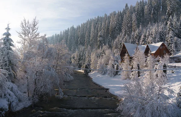 Casa de madera en la orilla del río en el bosque de montaña nevado en invierno — Foto de Stock