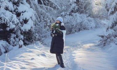 Güzel karlı ormanda bir kadın ve elinde bir buket çam ağacı dalı tutuyor.
