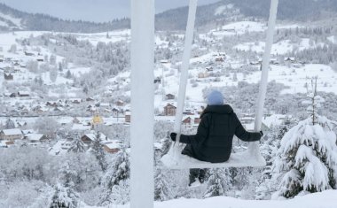 Salıncakta sallanan bir kadının panoramik görüntüsü karlı kasabayı izliyor.