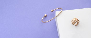 Panoramic shot of golden with diamonds bracelet and ring on white and purple background with copy space