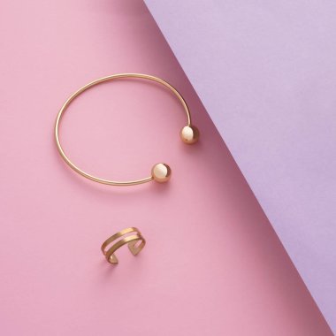 Altın bilezik ve yüzüğün üst görüntüsü eğimli pembe ve mor kağıt üzerinde kopya alanı ile