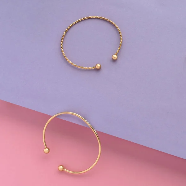 Top view of two golden bracelets on pink and purple slanted paper background — стоковое фото