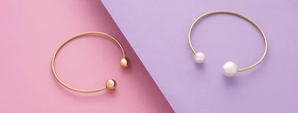 Panoramic shot of Two modern golden with pearls bracelets on pink and purple slanted background — стоковое фото