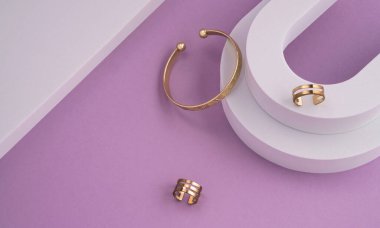 Modern altın bileziğin geometrik düz yüzeyinin üst görüntüsü ve kopyalama alanı olan beyaz ve mor arkaplan halkaları