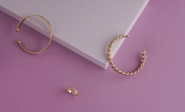 Geometrik ve zincir şekilli altın bilezikler ve pembe ve beyaz arka planda kopyalama alanı olan yüzük