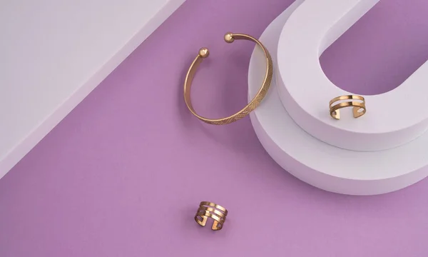 Widok z góry geometryczne płaskie układy nowoczesnej złotej bransoletki i pierścienie na białym i fioletowym tle z miejsca kopiowania — Zdjęcie stockowe