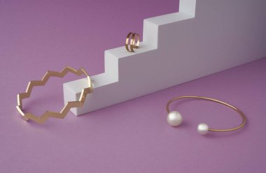 Altın zigzag şekil ve inci altın bilezikler ve mor arka planda beyaz podyumda yüzük.