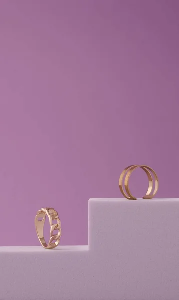 Pionowe ujęcie dwóch nowoczesnych złotych pierścieni na białym podium na fioletowym tle z przestrzenią do kopiowania — Zdjęcie stockowe