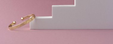 Geometrik desen tasarım bileziği beyaz merdiven podyumunda, pembe arka planda fotokopi alanı ile.
