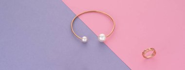 Modern gold bracelet and ring on pink and purple background with copy space