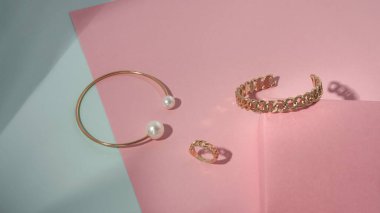 İnci ve zincir şekilli bilezikleri ve pastel renklerde yüzüğü olan altın rengi.