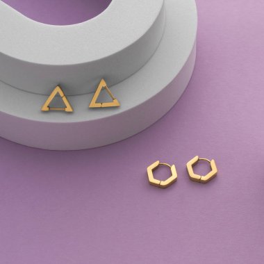 Geometrik küpelerin üst görünümü beyaz podyumda, mor zemin üzerinde kopya alanı ile birlikte.