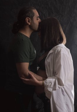 Romantik bir çiftin karanlık portresi, Orta Doğulu bir adam hamile karısına sarılıyor.