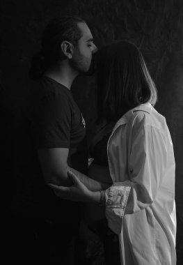 Hamile karısını kucaklayan bir adamın siyah beyaz portresi.