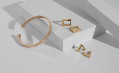 Altın bilezik ve geometrik küpeler beyaz podyumda fotokopi alanı ile