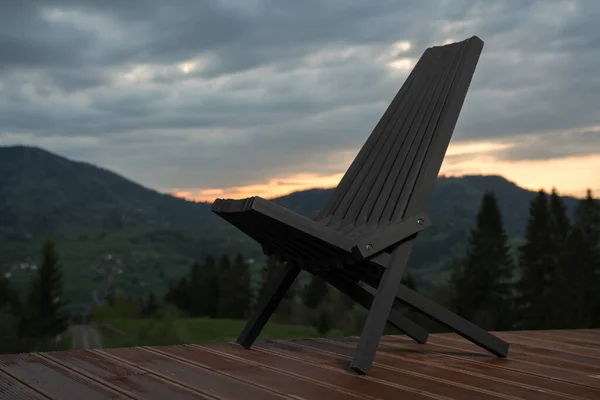 Black wooden patio chair on terrace with mountain view at cloudy sunset