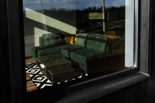 View of modern green couch from window from outside with mountain refliction on glass