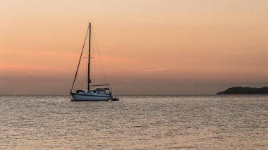 Bir yelkenli gün batımında demirler ve bir adam kıç tarafında, Vejle, Danimarka, 4 Eylül 2021 'de bir pencerede durur.