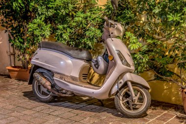 Yeşil yapraklı bir duvar boyunca duran Retro beyaz scooter, Girit, Yunanistan, 15 Ekim 2021