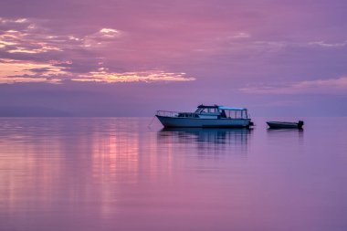 motor boat with dinghy lying at anchor in the pink mirror gloss sunrise, Vejle, Denmark, August 4, 2022