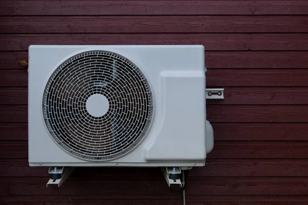 save electricity consumption with a white heat pump unit mounted on a red wood panel, Denmark, September 22, 2022