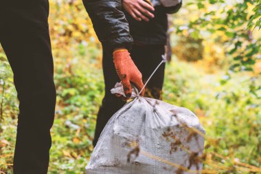 Adam ormandan bir torba çöp topluyor..