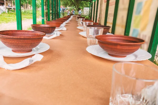 Clay plates on a long table in an outdoor dining area.