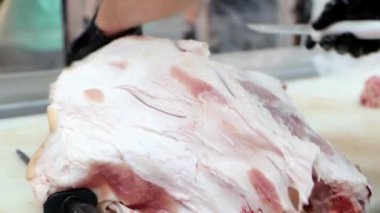 Profesyonel kasap et işleme tesisinde keskin bıçakla deriyi çiğ domuz etinden ayırır. Kasap dükkanı ve et endüstrisi konseptinde çalışma süreci, 4K video yakın çekim