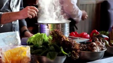 Şef ticari mutfakta çorba pişirirken tavadan çıkan buhar. Tavanın etrafında bir sürü farklı sebze var, yakın plan 4K.