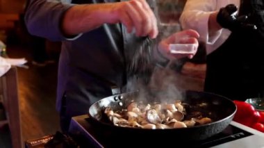 İki tanınmayan şef aşçılık sınıfında yemek hazırlıyor. Pişirme tavasında tuzlu mantar pişirir ve karıştırır, yakın çekim 4k video.
