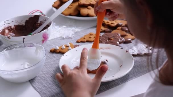 Kid girl decorates xmas tree shaped cookie with white icing by culinary brush — Stock video