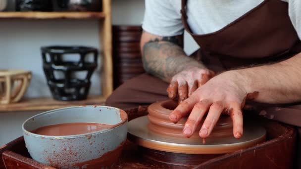 エプロンの男性陶芸家は 回転する陶芸家の車輪の上の粘土からセラミック料理を作っています クローズアップ手4K — ストック動画