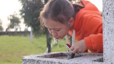 Şehir parkındaki çeşmede su içen bir kızın portresi, 4K görüntü.