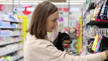 Küçük kucak köpeği olan genç bir kadın, süpermarket hayvan departmanından yemek seçiyor, 4K görüntü..