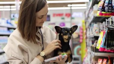 Süpermarkette kucağında küçük bir köpekle genç bir kadının portresi. Sahibi bir köpek besliyor, 4K görüntü..