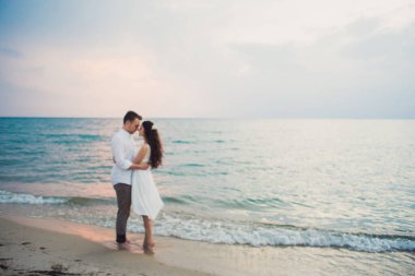 Beyaz elbiseli, sevecen erkek ve kız el ele tutuşurken arka plan bulanıklaşıyor.