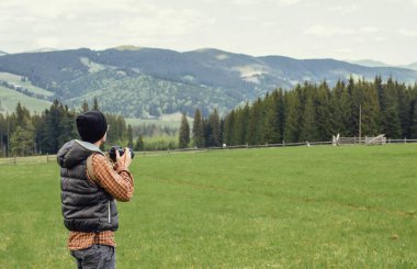 Genç bir adam dağlarda kamerayla gezer.