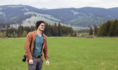 Genç bir adam dağlarda kamerayla gezer.