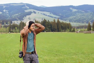 Genç bir adam dağlarda kamerayla gezer.